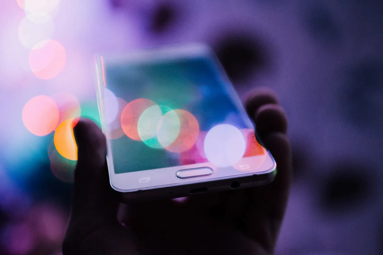 Main tenant un smartphone devant des reflets lumineux colorés