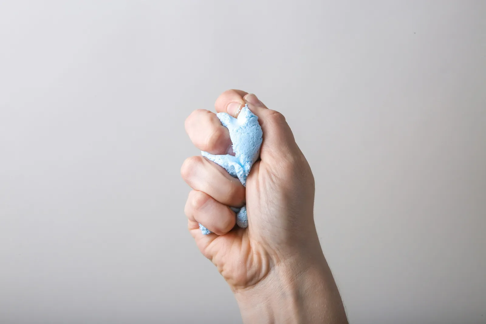 Main qui serre un petit objet souple bleu clair sur fond gris